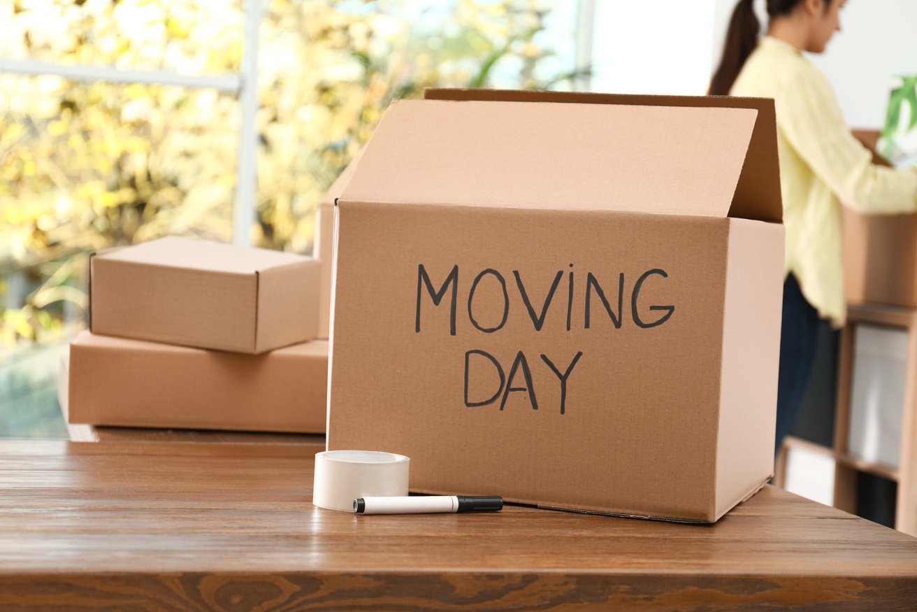 Cardboard Box with Words MOVING DAY and Packaging Items on Woode